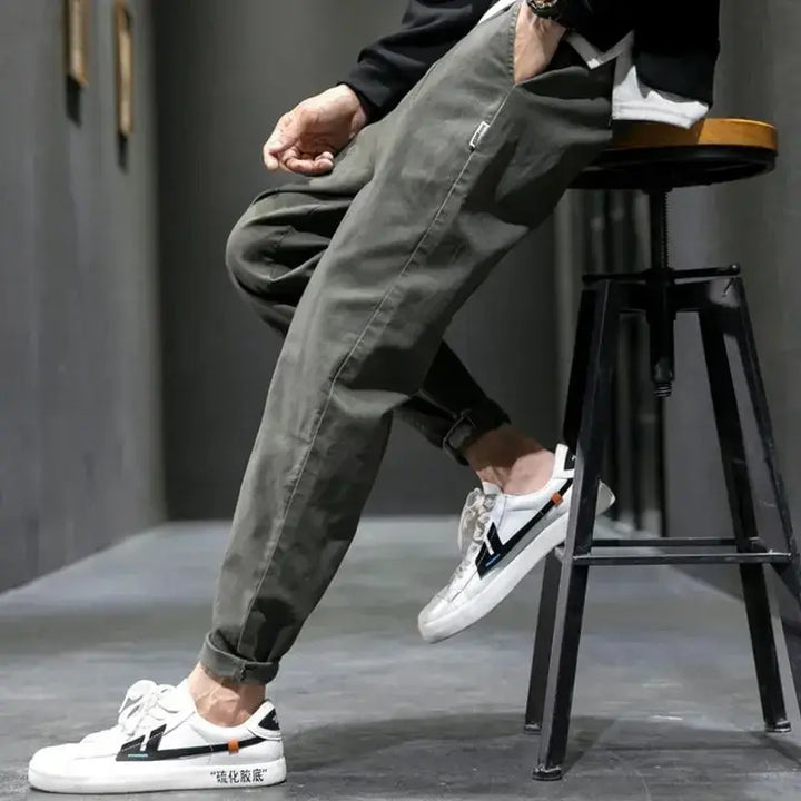 Person wearing green pants and white sneakers sitting on a stool.