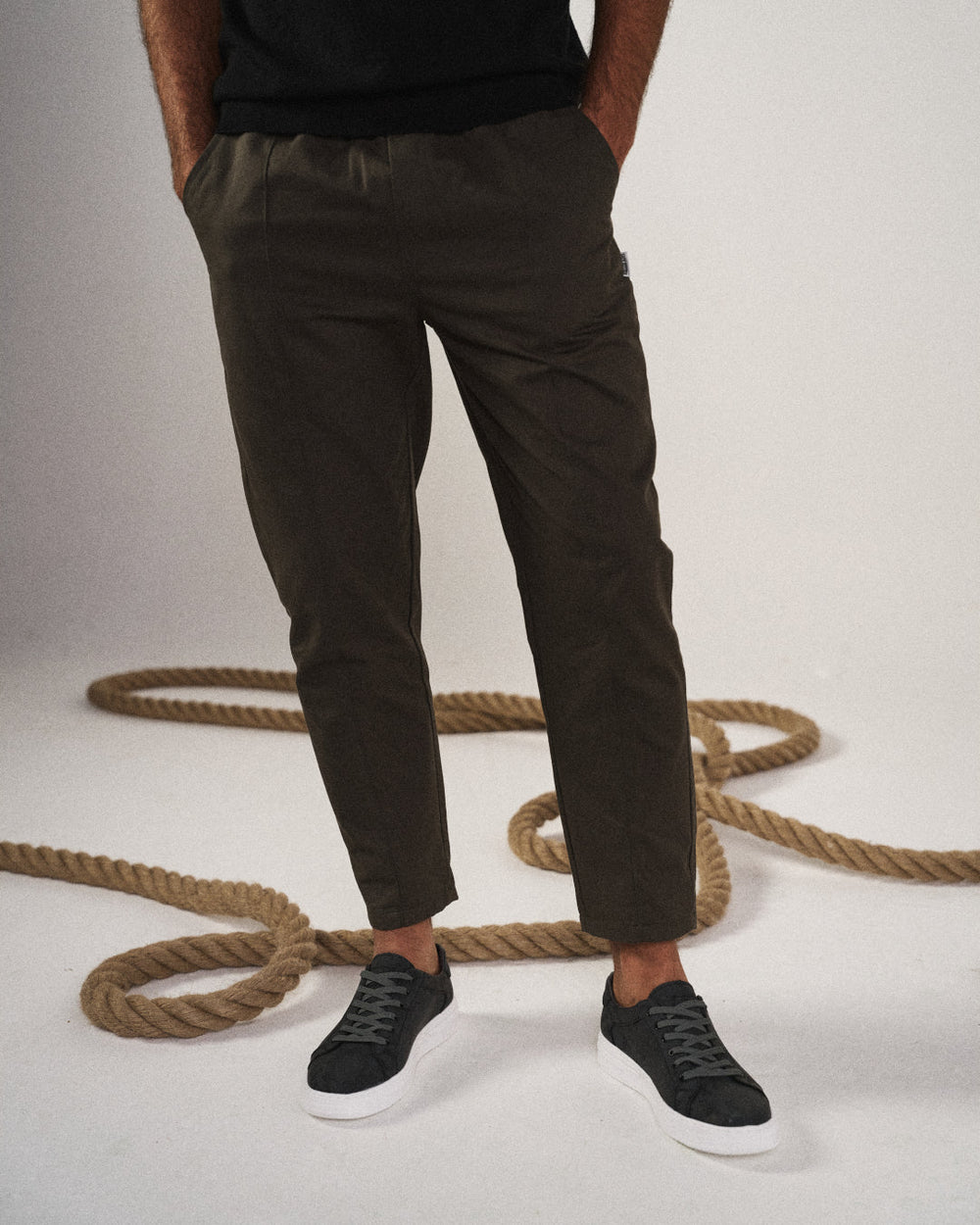Person wearing dark pants and black shoes standing next to a rope on a light background